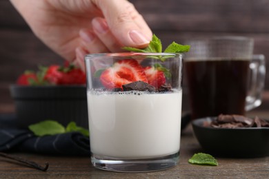Photo of Woman decorating tasty panna cotta with mint at wooden table, closeup