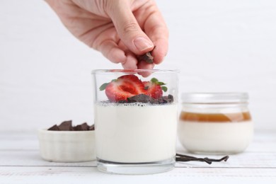 Photo of Woman adding chocolate piece to tasty panna cotta at white wooden table, closeup