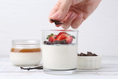 Photo of Woman adding chocolate pieces to tasty panna cotta at white wooden table, closeup