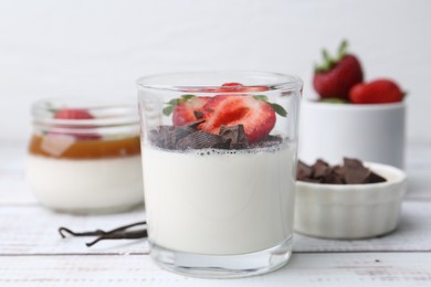 Photo of Tasty panna cotta with chocolate, strawberries and vanilla on white wooden table, closeup