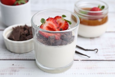 Photo of Tasty panna cotta with chocolate, strawberries and vanilla on white wooden table, closeup
