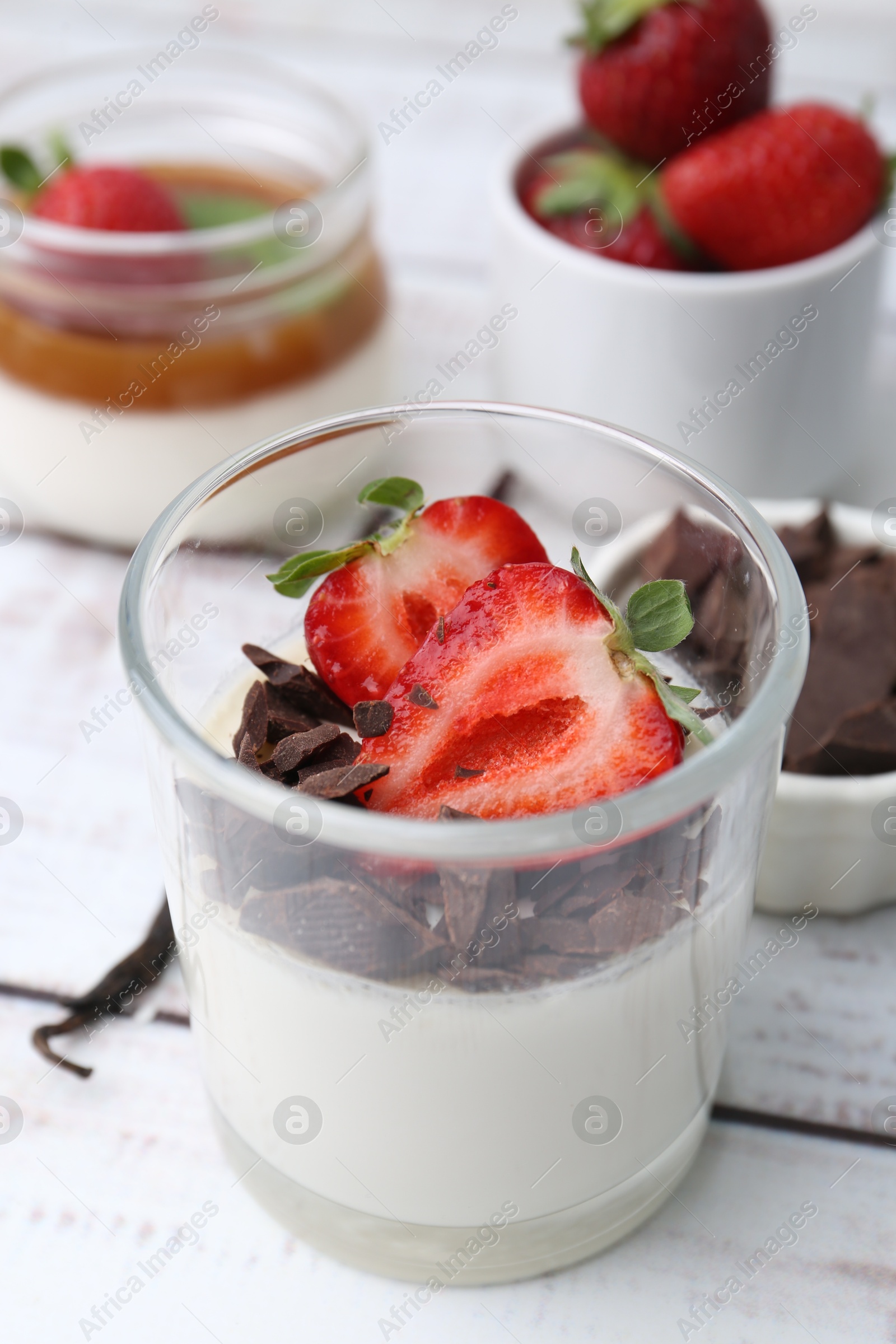 Tasty panna cotta with chocolate, strawberries and vanilla on white wooden table, closeup Photo of Tasty panna cotta with chocolate, strawberries and vanilla on white wooden table, closeup