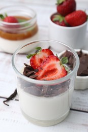 Photo of Tasty panna cotta with chocolate, strawberries and vanilla on white wooden table, closeup