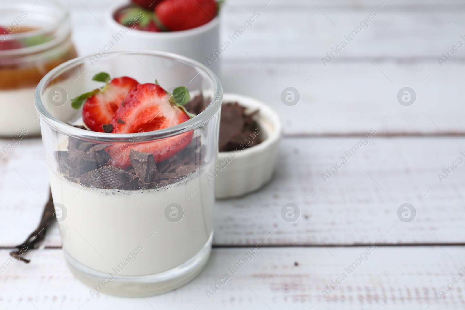 Photo of Tasty panna cotta with chocolate, strawberries and vanilla on white wooden table, closeup. Space for text