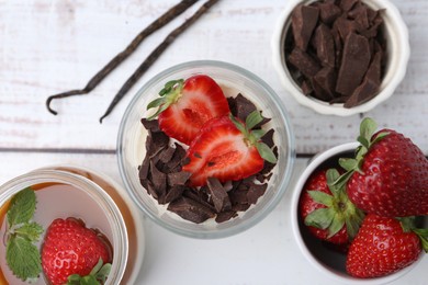 Photo of Tasty panna cotta with chocolate, strawberries, vanilla pods and caramel on white wooden table, flat lay
