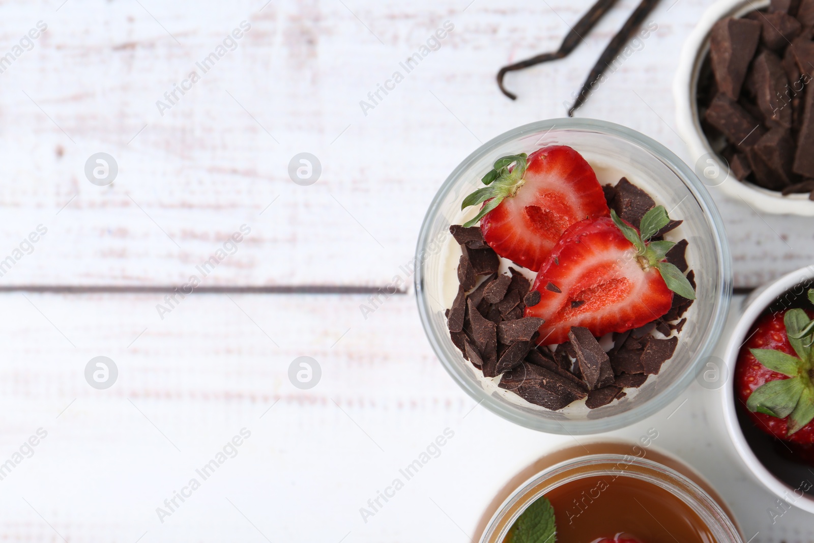 Tasty panna cotta with chocolate, strawberries, vanilla and caramel on white wooden table, flat lay. Space for text Photo of Tasty panna cotta with chocolate, strawberries, vanilla and caramel on white wooden table, flat lay. Space for text