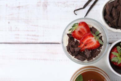 Photo of Tasty panna cotta with chocolate, strawberries, vanilla and caramel on white wooden table, flat lay. Space for text