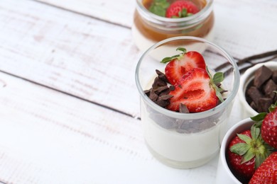 Photo of Tasty panna cotta with chocolate, strawberries, vanilla pods and caramel on white wooden table, closeup. Space for text