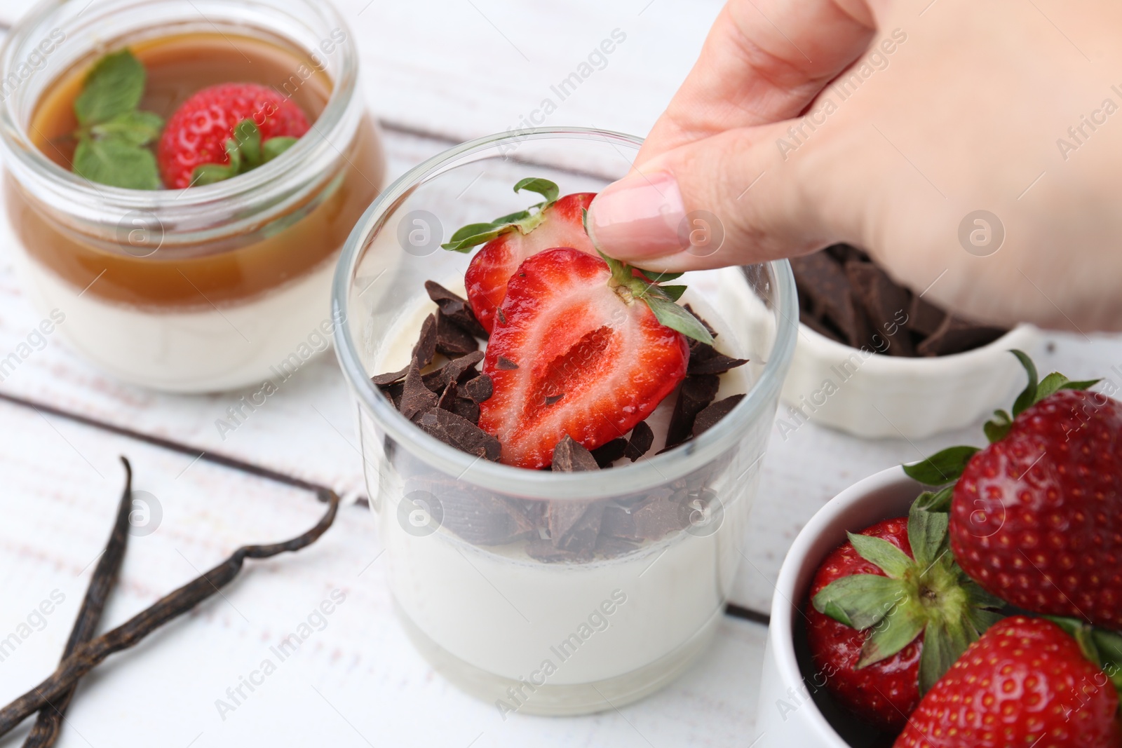 Woman adding strawberry to tasty panna cotta at white wooden table, above view Photo of Woman adding strawberry to tasty panna cotta at white wooden table, above view