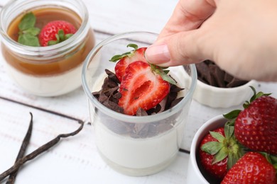 Photo of Woman adding strawberry to tasty panna cotta at white wooden table, above view