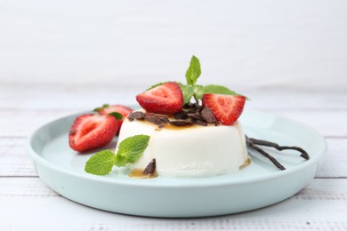 Photo of Tasty panna cotta with chocolate, strawberries, mint, caramel and vanilla pods on white wooden table, closeup