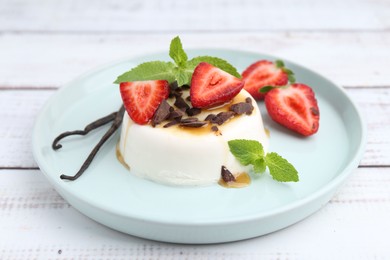Photo of Tasty panna cotta with chocolate, strawberries, mint, caramel and vanilla pods on white wooden table, closeup