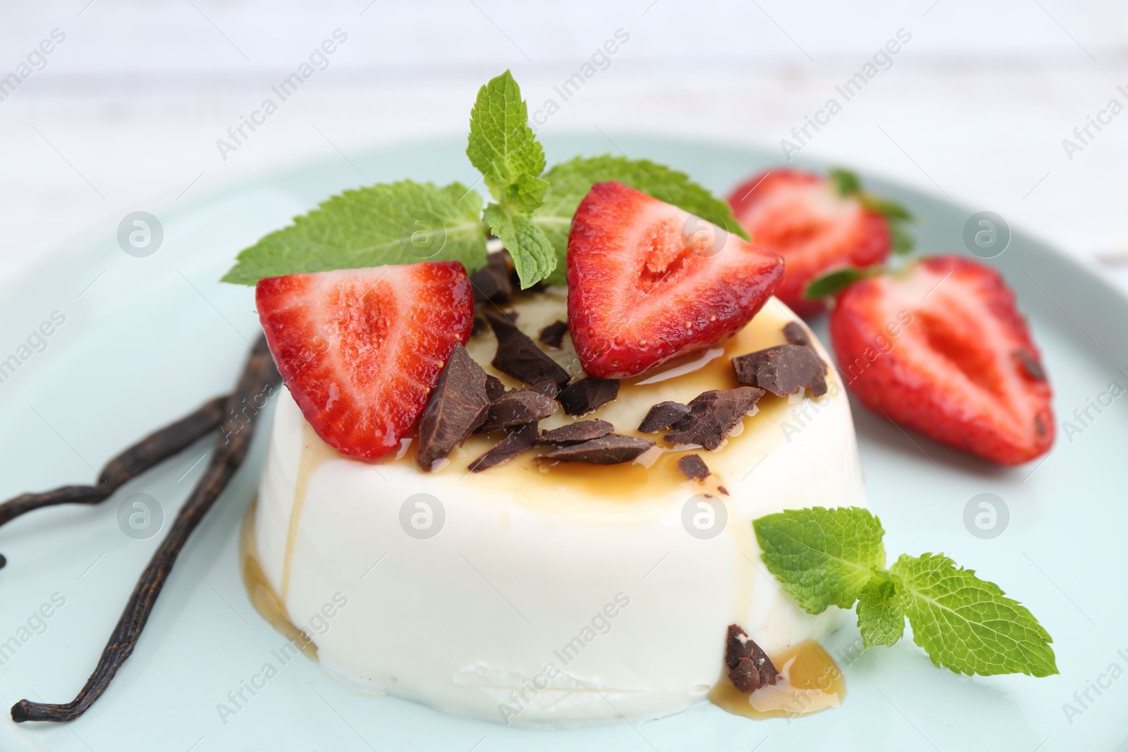 Tasty panna cotta with chocolate, strawberries, mint, caramel and vanilla pods on table, closeup Photo of Tasty panna cotta with chocolate, strawberries, mint, caramel and vanilla pods on table, closeup