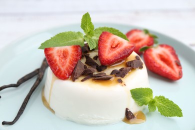 Photo of Tasty panna cotta with chocolate, strawberries, mint, caramel and vanilla pods on table, closeup