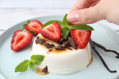 Photo of Woman adding strawberry to tasty panna cotta at table, closeup