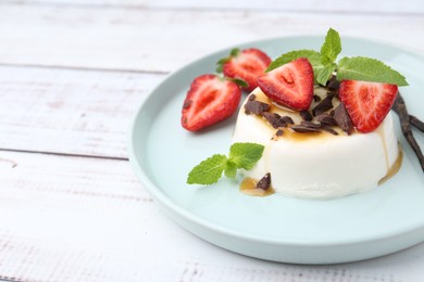 Photo of Tasty panna cotta with chocolate, strawberries, mint, caramel and vanilla pods on white wooden table, closeup. Space for text