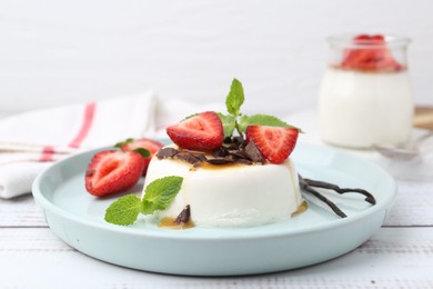 Photo of Tasty panna cotta with chocolate, strawberries, mint, caramel and vanilla pods on white wooden table, closeup
