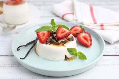 Photo of Tasty panna cotta with chocolate, strawberries, mint, caramel and vanilla pods on white wooden table, closeup