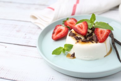 Photo of Tasty panna cotta with chocolate, strawberries, mint, caramel and vanilla pods on white wooden table, closeup. Space for text