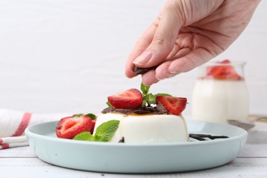 Photo of Woman adding chocolate pieces to tasty panna cotta at white wooden table, closeup