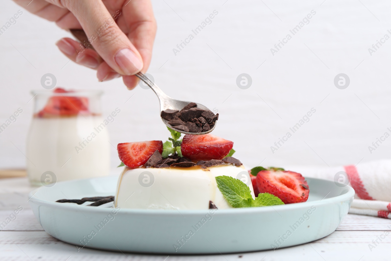 Woman adding chocolate pieces to tasty panna cotta at white wooden table, closeup Photo of Woman adding chocolate pieces to tasty panna cotta at white wooden table, closeup