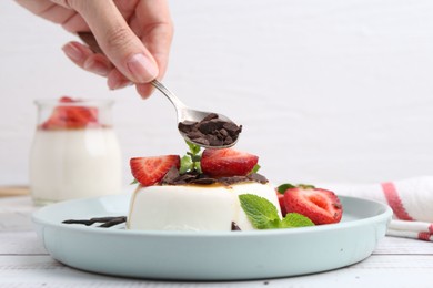 Photo of Woman adding chocolate pieces to tasty panna cotta at white wooden table, closeup