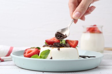 Photo of Woman adding chocolate pieces to tasty panna cotta at white wooden table, closeup