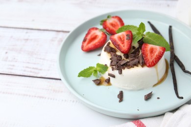 Photo of Tasty panna cotta with chocolate, strawberries, mint, caramel and vanilla on white wooden table, closeup. Space for text