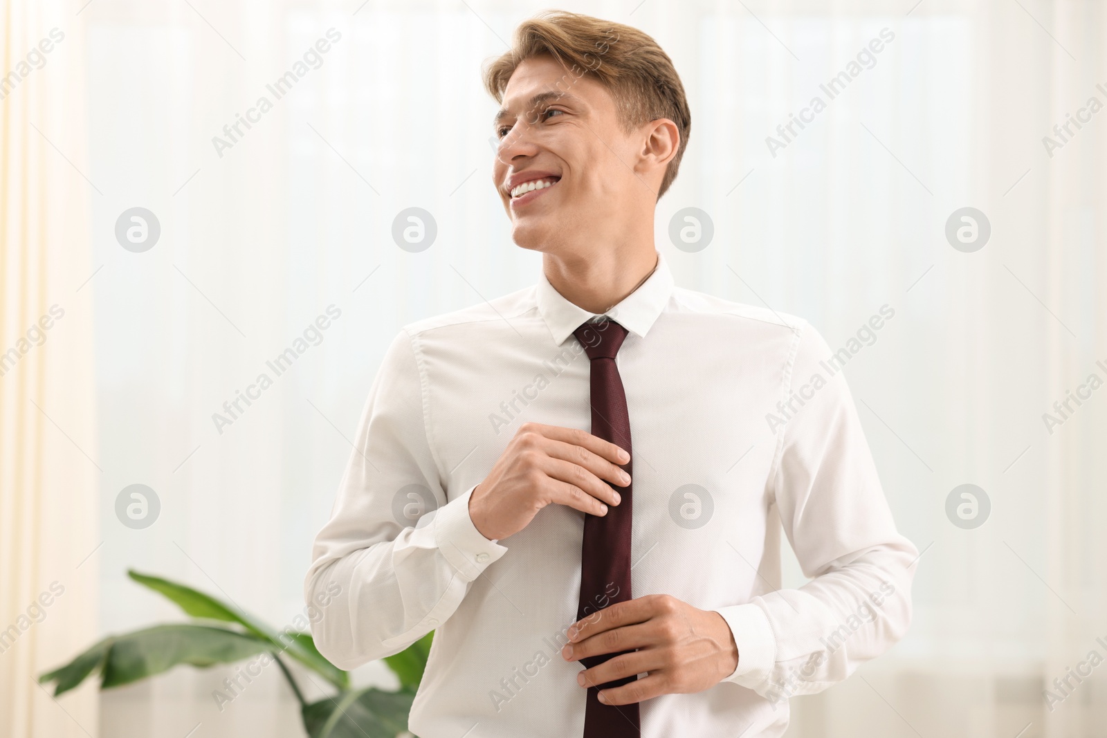 Photo of Man tying stylish brown necktie at home