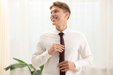Photo of Man tying stylish brown necktie at home