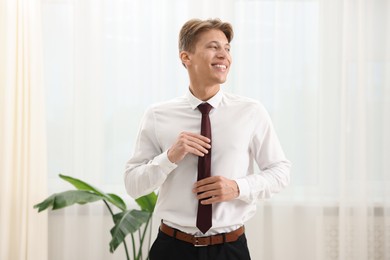 Photo of Man tying stylish brown necktie at home