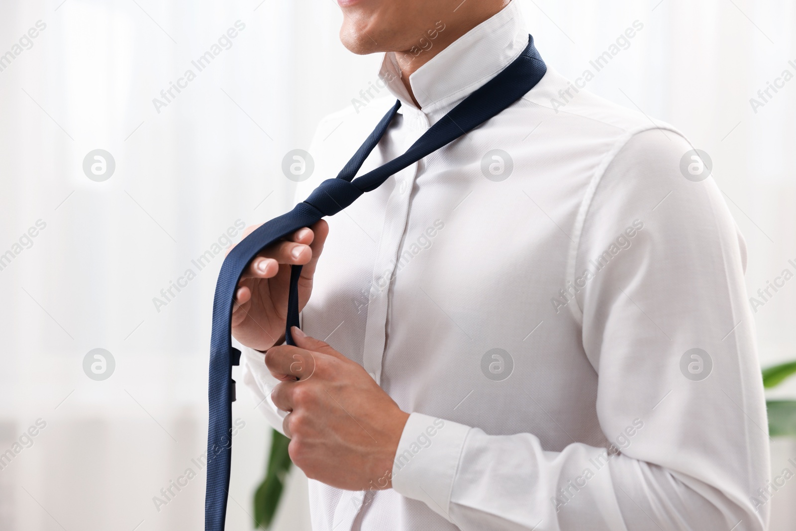 Photo of Man tying stylish necktie at home, closeup
