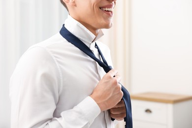 Photo of Man tying stylish necktie at home, closeup