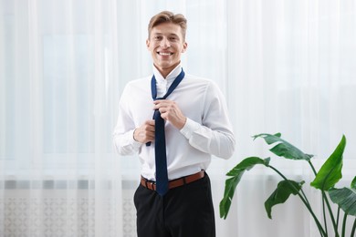 Photo of Man tying stylish blue necktie at home
