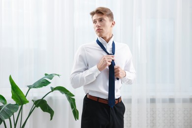 Photo of Man tying stylish blue necktie at home