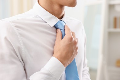 Photo of Man tying stylish necktie at home, closeup