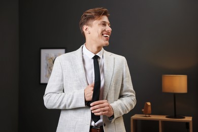 Photo of Man tying stylish black necktie at home
