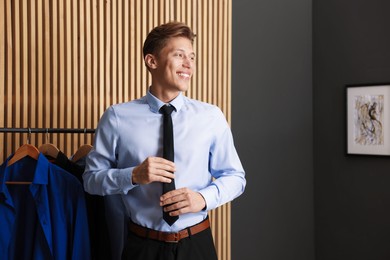 Photo of Man tying stylish black necktie at home