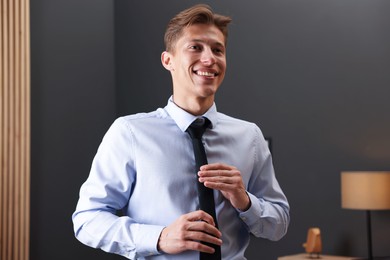 Photo of Man tying stylish black necktie at home
