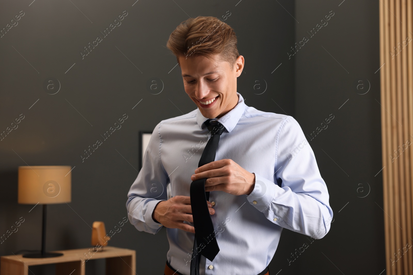 Photo of Man tying stylish black necktie at home