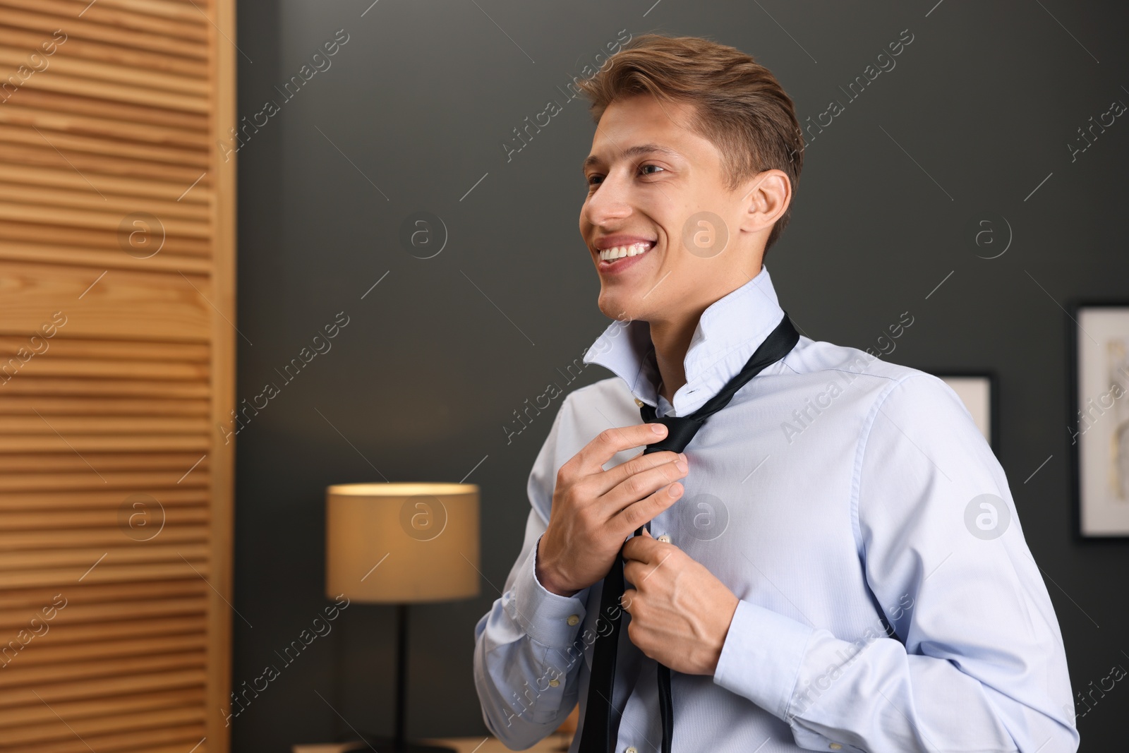 Photo of Man tying stylish black necktie at home