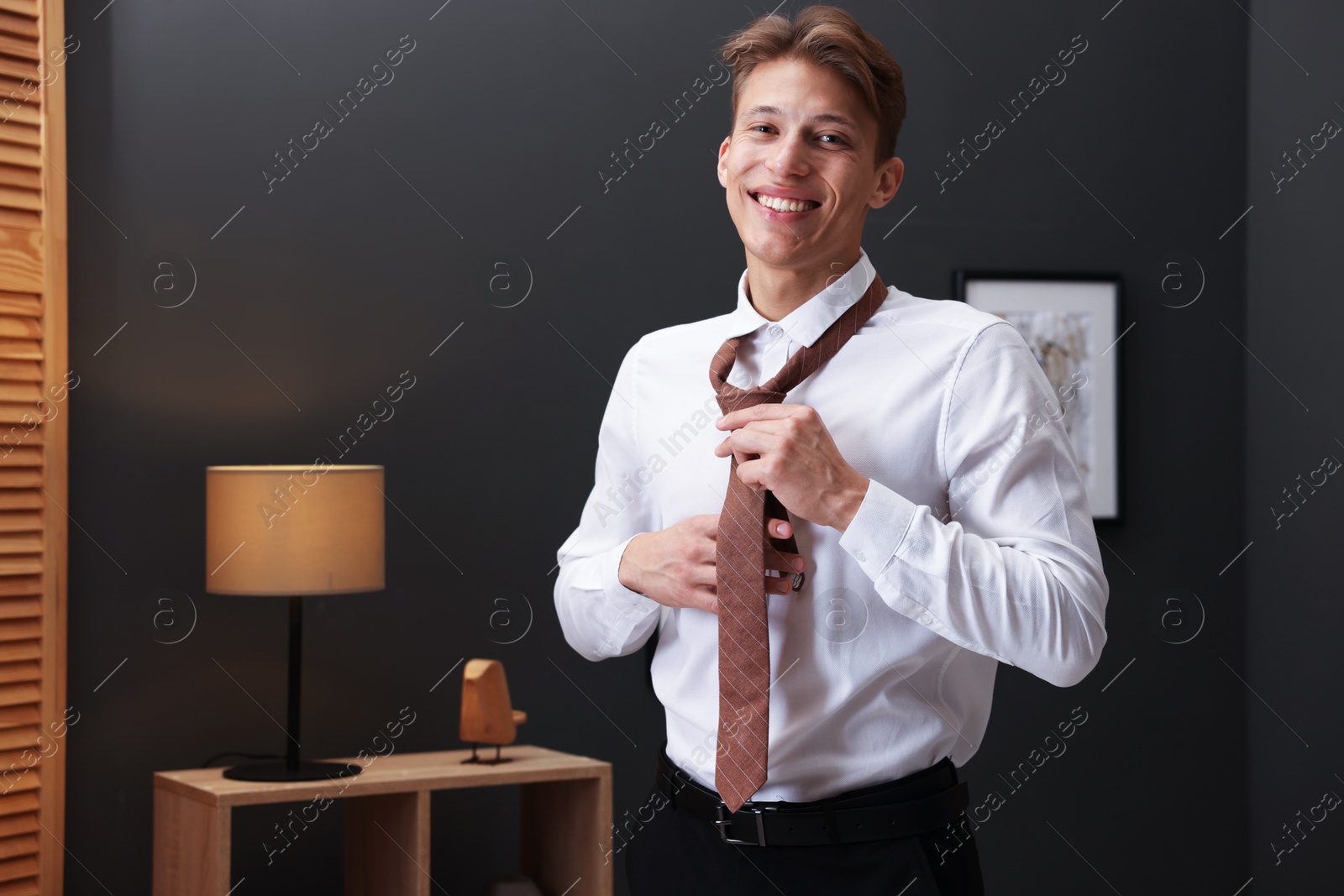 Photo of Man tying stylish brown necktie at home
