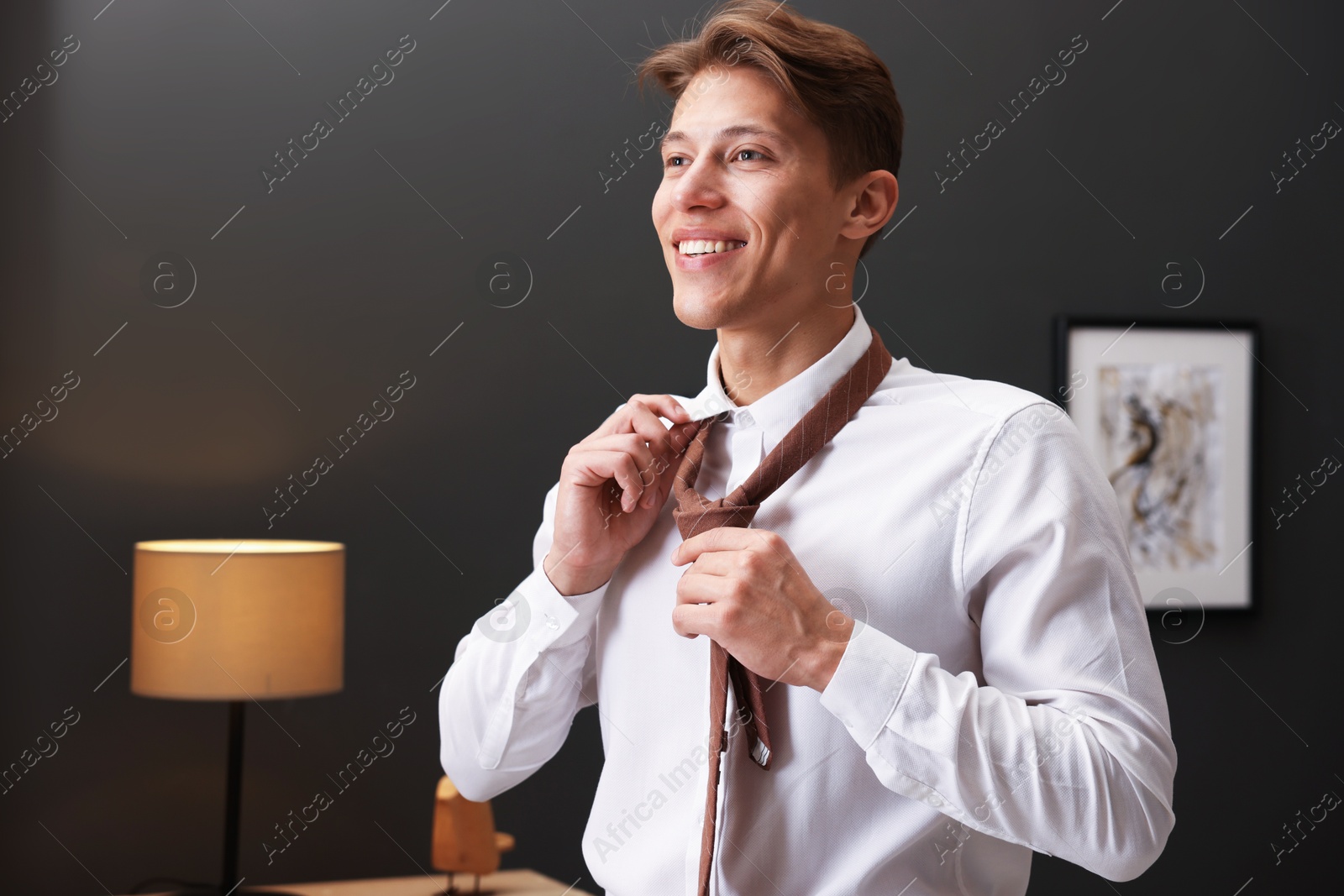 Photo of Man tying stylish brown necktie at home
