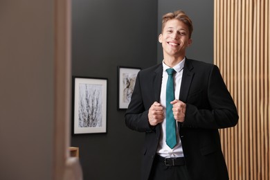 Photo of Man tying stylish green necktie at home