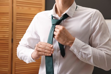 Photo of Man tying stylish necktie at home, closeup