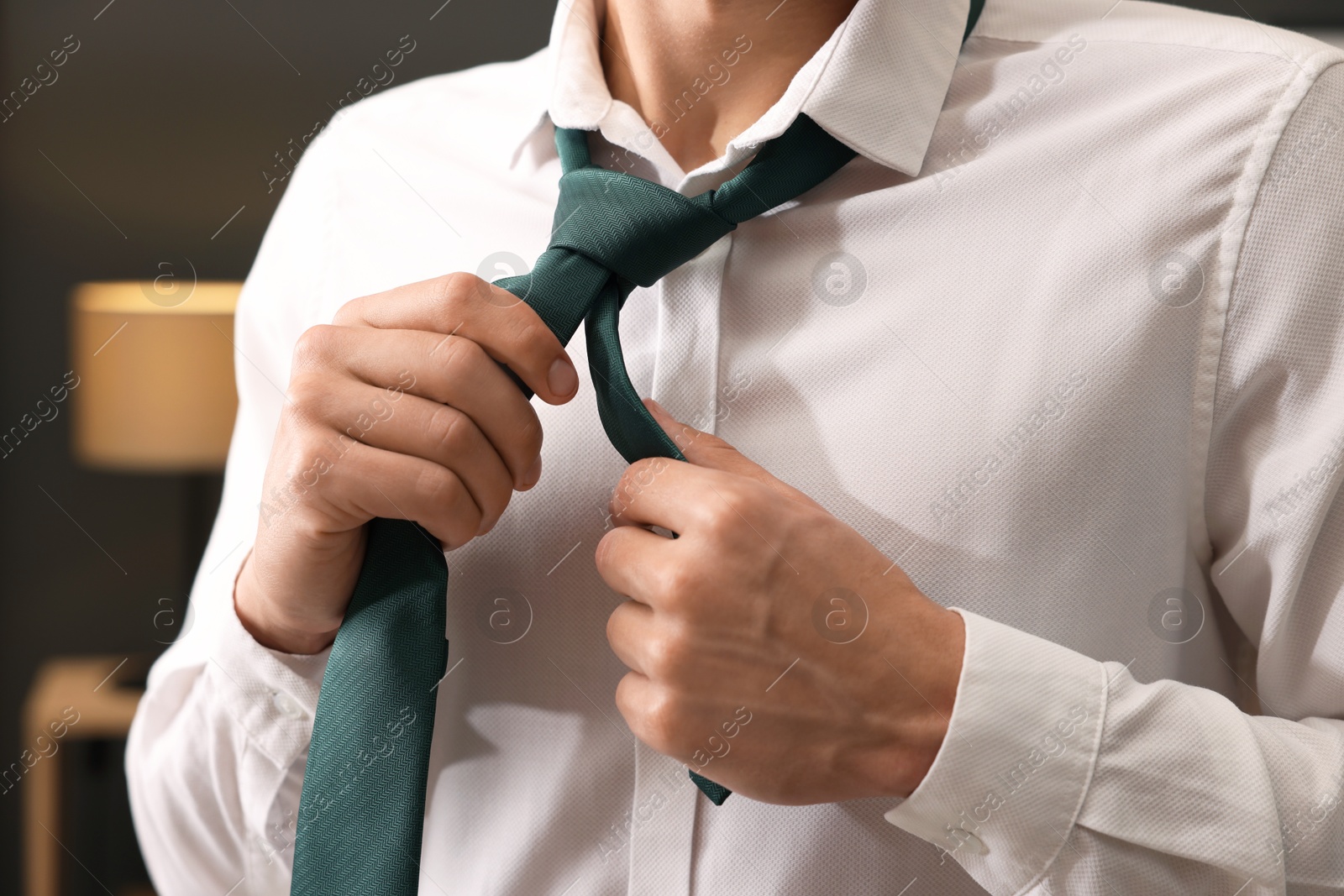 Photo of Man tying stylish necktie at home, closeup