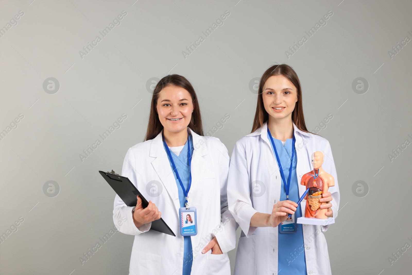 Photo of Medical students with human body model and clipboard on light grey background