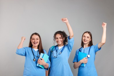 Photo of Group of excited medical students with books on light grey background
