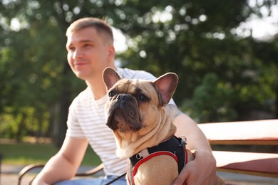 Photo of Happy man with his cute French bulldog on bench in park, selective focus