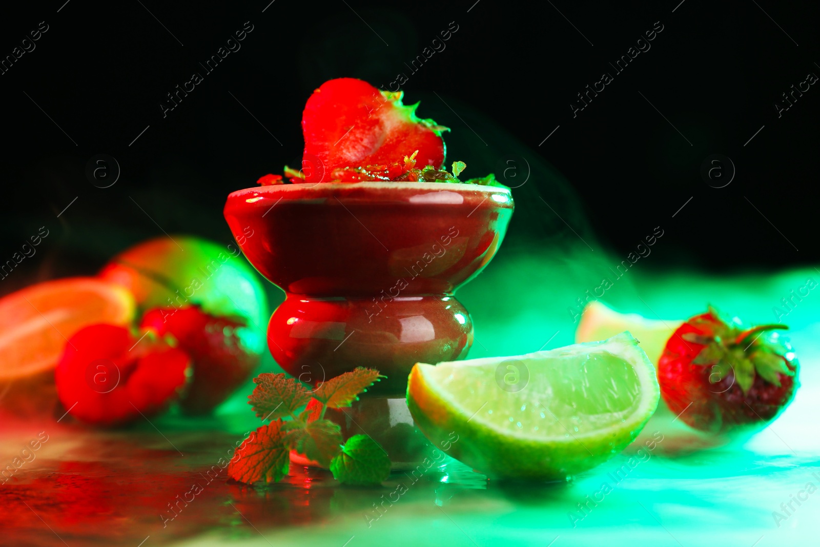 Photo of Hookah bowl with limes, strawberries, mint and smoke on black table, closeup